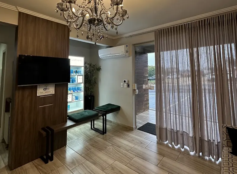 Recepção da clínica com lustre de cristal, TV e bancos verdes